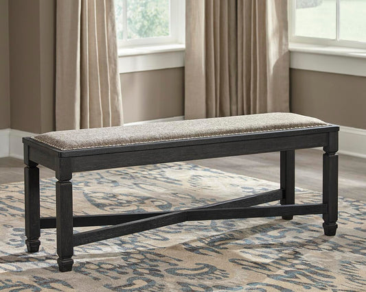 The Tyler Creek Upholstered Bench, with its cushioned seat, sits atop a patterned rug in a bright room with beige walls and curtains, adding urban farmhouse charm to the space.