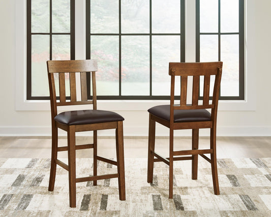 Two Ralene Upholstered Barstools with slatted backs and dark cushions are placed on a patterned rug in front of large windows.