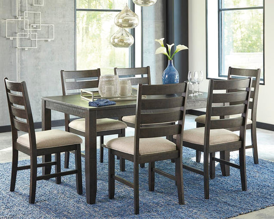 A modern dining room showcases the Rokane Dining Room Table Set (7/CN) with six beige upholstered chairs, a blue rug, pendant lighting, and a blue vase filled with white flowers.