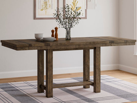 The Moriville RECT DRM Counter EXT Table, topped with a vase of branches, dishes, and salt and pepper shakers, stands on a plaid rug in a bright room.