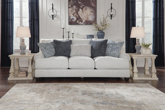 A neutral-toned living room with a light gray sofa, decorative pillows, two matching side tables with lamps, the Ogaleesha Wall Sconce in bronze-tone metal, and wall art above the sofa.