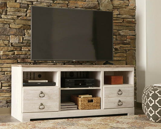 A flat-screen TV sits on the Willowton LG TV Stand w/Fireplace Option, featuring drawers, shelves with electronics and a basket, positioned against a stone wall.