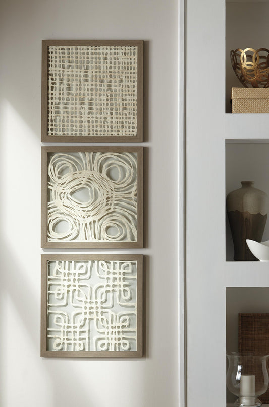The Odella Wall Decor Set (3/CN) features three square framed abstract art pieces with geometric neutral patterns, vertically arranged on a white wall for striking modern decor beside shelves with decorative objects.