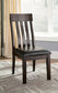 A Haddigan Dining UPH Side Chair (2/CN) with a dark wood frame and black faux leather upholstered seat sits on a patterned rug by a window with beige curtains.