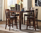 The Bennox DRM Counter Table Set (5/CN), featuring a wooden counter-height table and four matching high-back chairs, sits on a gray rug adorned with decorative items, bowls, and wine glasses near bright windows.