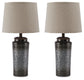 A pair of Norbert Metal Table Lamps featuring textured dark metal bases and light beige fabric lampshades, evoking modern sophistication, are displayed against a white background.