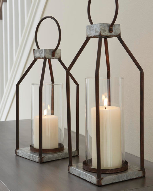 The Diedrick Lantern Set (2/CN), featuring glass enclosures and white pillar candles, casts a warm glow on a wooden surface beside the staircase—an elegant indoor-outdoor candle holder lantern duo.