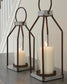 The Diedrick Lantern Set (2/CN), featuring glass enclosures and white pillar candles, casts a warm glow on a wooden surface beside the staircase—an elegant indoor-outdoor candle holder lantern duo.