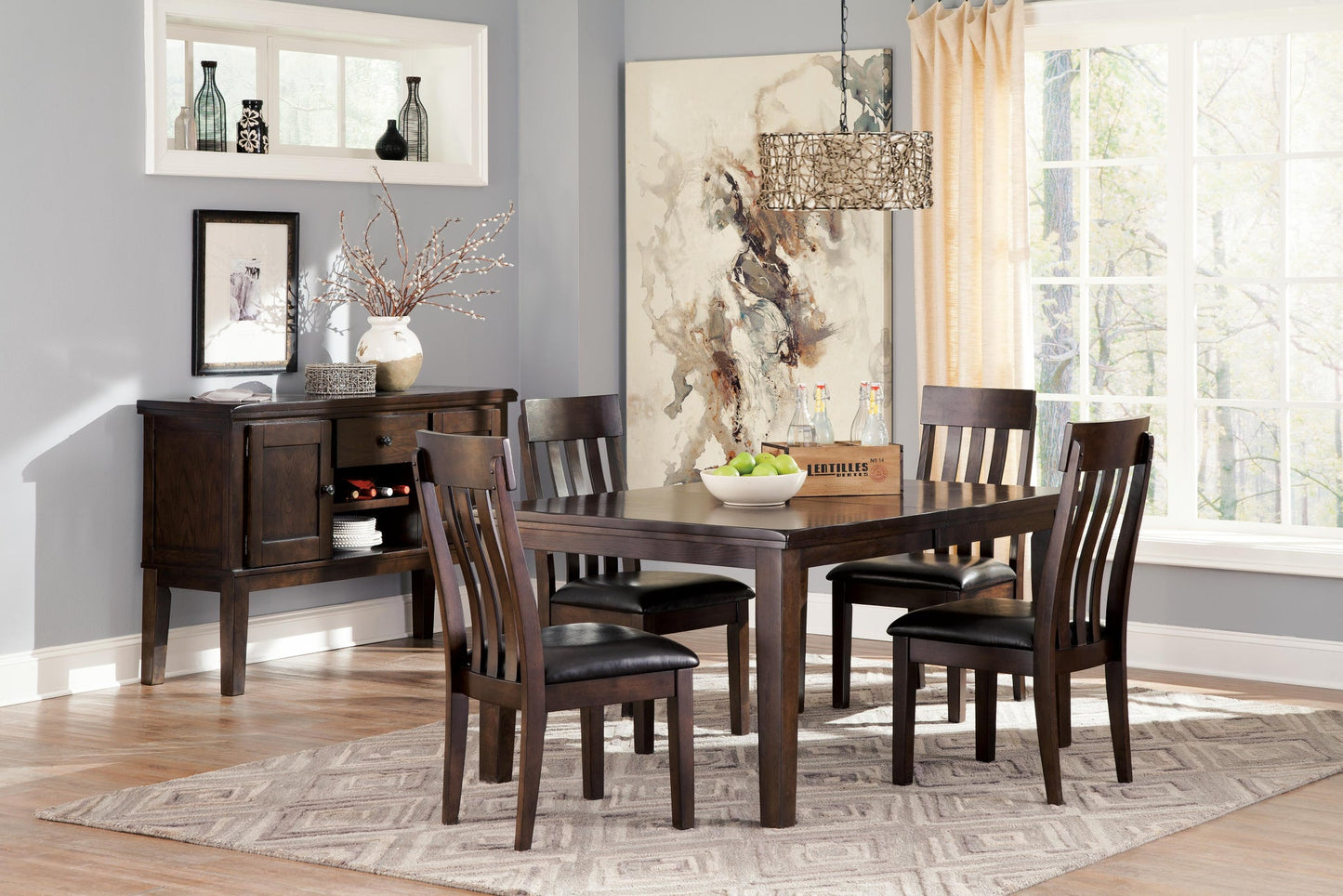 A dining room featuring the Haddigan RECT Dining Room EXT Table seating up to 8, six chairs on a patterned rug, a sideboard with decor, wall art, and large windows dressed in light curtains.