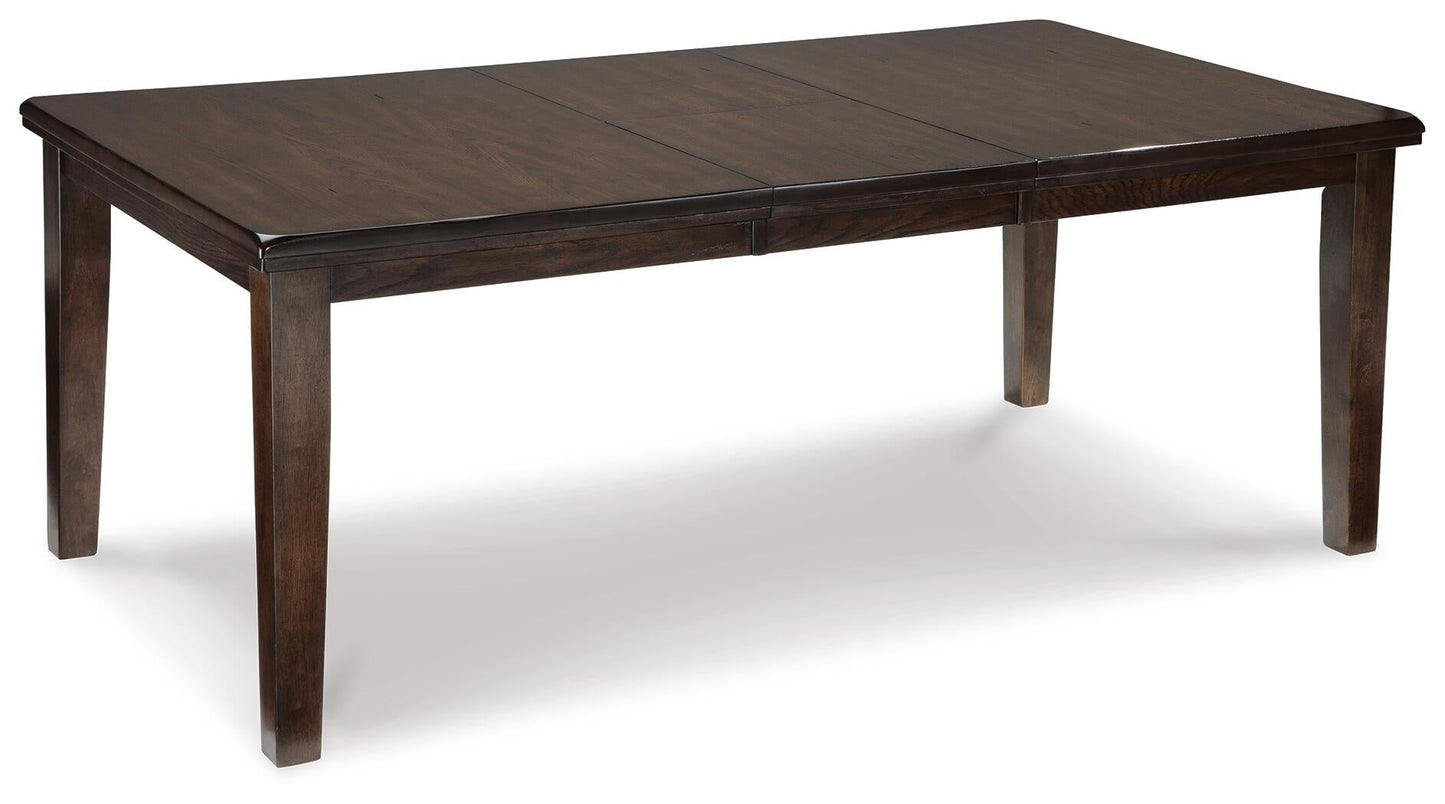The Haddigan RECT Dining Room EXT Table is a rectangular dark wood farmhouse table with four legs, a smooth surface, and a butterfly leaf extension. Shown on a white background, it seats up to 8 for versatile gatherings.