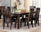 The Haddigan RECT Dining Room EXT Table, shown with six matching chairs, a bowl of green apples, and glass bottles atop a patterned rug in a bright room with large windows, features a butterfly leaf extension to seat up to 8.