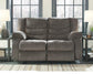 The Tulen Reclining Loveseat in gray chenille sits between two side tables with lamps, positioned in front of large black-framed windows.