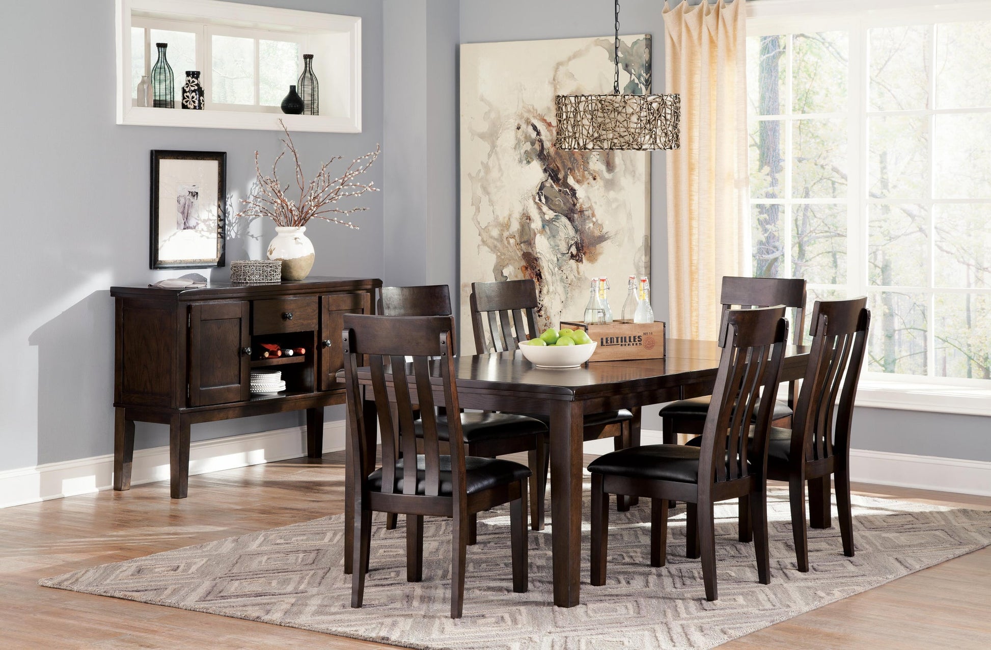 A dining room featuring the Haddigan RECT Dining Room EXT Table with butterfly leaf, six chairs, a sideboard with decor, modern chandelier, large artwork, and a window with curtains letting in natural light. Seats up to 8.