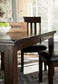 The Haddigan RECT Dining Room EXT Table, a dark wood farmhouse style with butterfly leaf extension, comes with two matching chairs. It’s shown in a sunlit room, topped with green apples and glass bottles in a wooden crate.