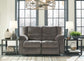 The Tulen Reclining Loveseat in soft gray chenille sits between two side tables with lamps and vases in a bright room featuring large windows and a geometric chandelier.