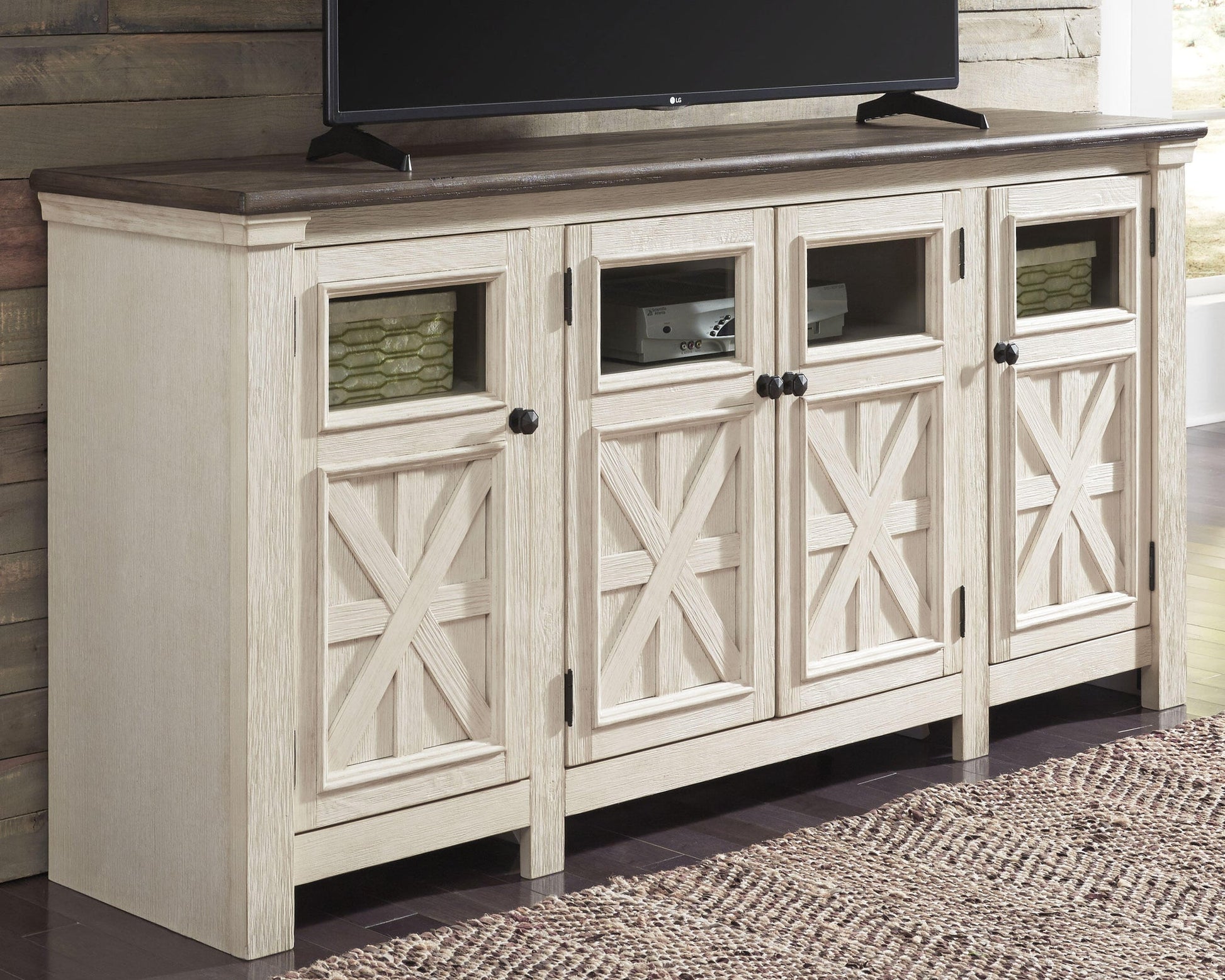 The Bolanburg Extra Large TV Stand features a two-tone farmhouse design with a dark top, four crisscross glass-panel cabinet doors, and black knobs. Store electronics and baskets neatly inside this stylish console.