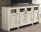 The Bolanburg Extra Large TV Stand features a two-tone farmhouse design with a dark top, four crisscross glass-panel cabinet doors, and black knobs. Store electronics and baskets neatly inside this stylish console.