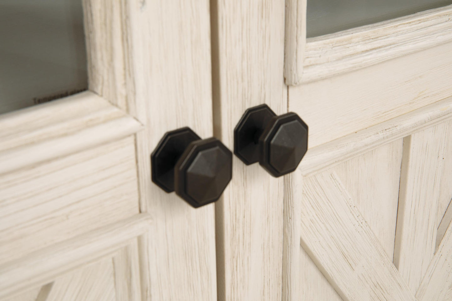 Close-up of two black, octagonal door knobs on white, rustic wooden cabinet doors—perfect farmhouse-style details found on the Bolanburg Extra Large TV Stand.
