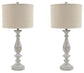 A pair of Bernadate Poly Table Lamps (2/CN) with beige drum shades and ornate candlestick-style bases in a distressed whitewash finish, displayed side by side against a white background.