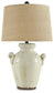 The Emelda Ceramic Table Lamp (1/CN) features a crackled white finish, two small handles, and a beige burlap shade, bringing effortless farmhouse charm to any space.