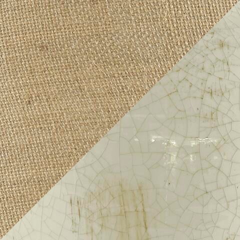 A diagonal split image shows coarse brown fabric on the upper left and the cracked, aged white surface of the Emelda Ceramic Table Lamp (1/CN) on the lower right, evoking a vintage aesthetic.