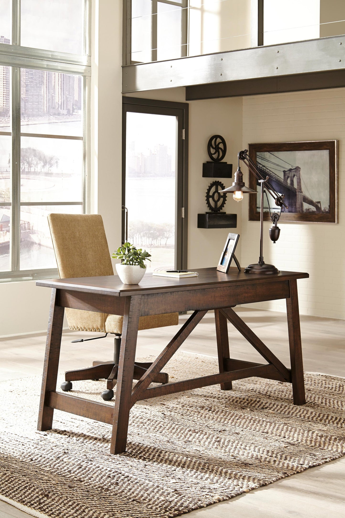 A modern office features the Baldridge Home Office Large Leg Desk, a rolling chair, desk lamp, potted plant, wall art, large windows, and rustic industrial decor.
