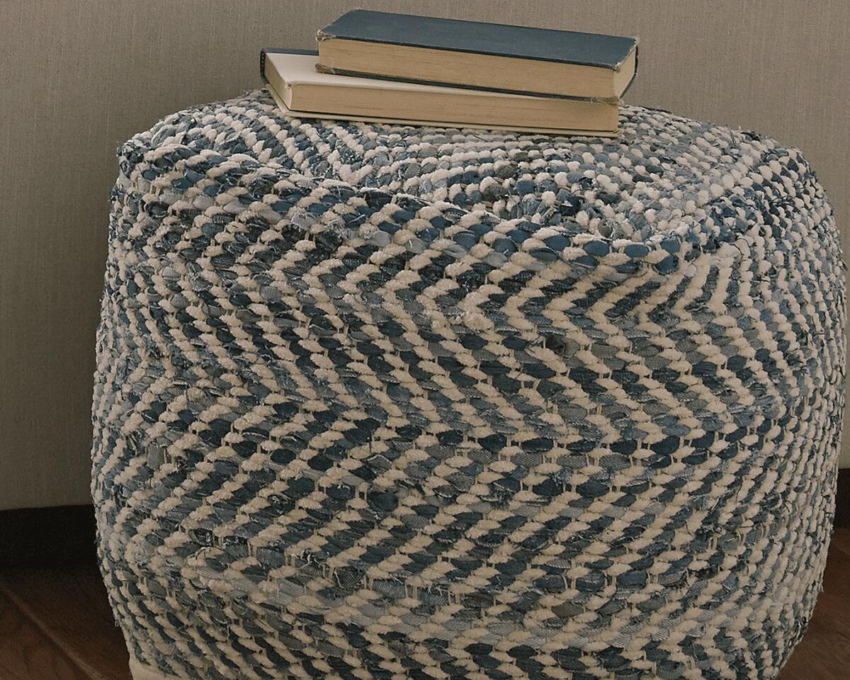 The Chevron Pouf, featuring a blue and white chevron design, is topped with three closed books and placed against a neutral-colored background.