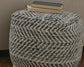 The Chevron Pouf, featuring a blue and white chevron design, is topped with three closed books and placed against a neutral-colored background.