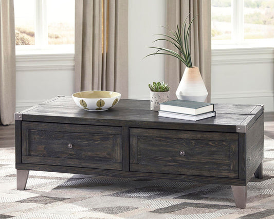 The Todoe Lift Top Cocktail Table, featuring dark wood and two drawers, is styled with a bowl, potted plant, vase with greenery, and two stacked books on a patterned rug for a rustic-industrial vibe.