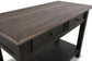 The Tyler Creek Sofa Table features a dark, weathered gray-brown finish with traditional hardware—two drawers, metal knobs, and a lower shelf—shown against a white background.