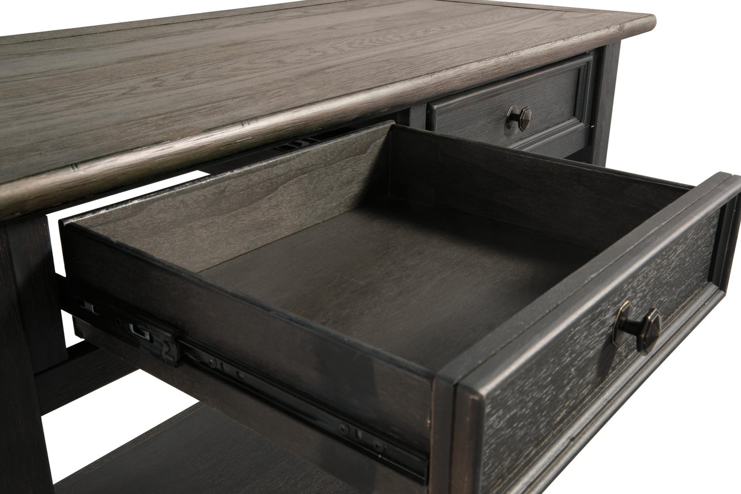 A close-up of the Tyler Creek Sofa Table shows its weathered gray-brown wood finish and an open dark wood drawer, highlighting traditional hardware on the metal slides.