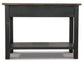 The Tyler Creek Sofa Table features a weathered gray-brown wood build with a dark finish, flat top surface, traditional hardware, and a lower storage shelf.