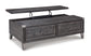 The Todoe Lift Top Cocktail Table features a rectangular weathered pine design with two drawers and a partially raised lift-top, revealing storage space underneath for a rustic-industrial look.