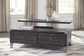 The Todoe Lift Top Cocktail Table, featuring a dark wood finish and two drawers, displays stacked books, a potted plant, and a vase. It's set in a bright room with large windows and beige curtains for a rustic-industrial look.