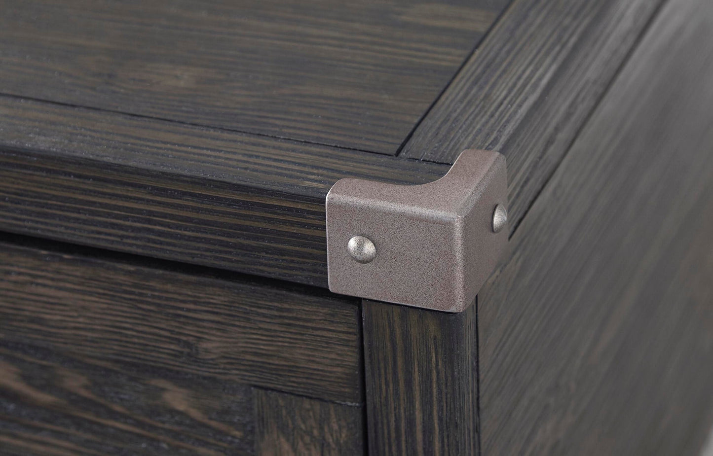 Close-up of the corner of the Todoe Lift Top Cocktail Table, featuring a weathered pine finish and a dark wooden box design with a metal corner bracket secured by two screws.