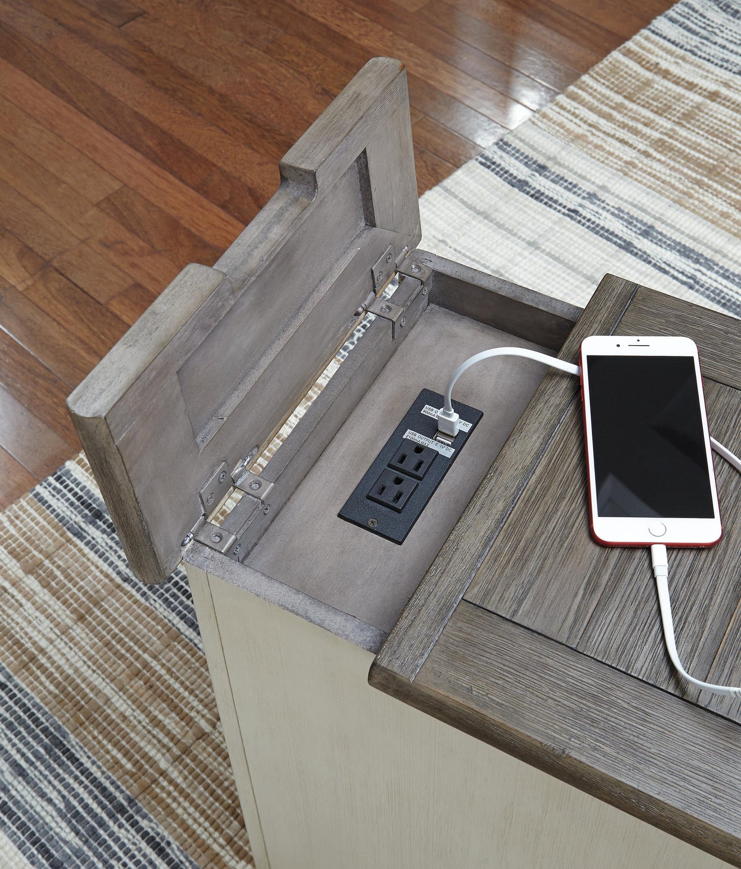 The Bolanburg Chair Side End Table in antique white offers an open compartment with two power outlets and two USB ports, perfect for charging devices like a smartphone via USB cable.