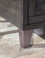 Close-up of the bottom corner of the Todoe Lift Top Cocktail Table, featuring a dark wood finish and tapered metallic leg, set on a neutral-toned textured rug.