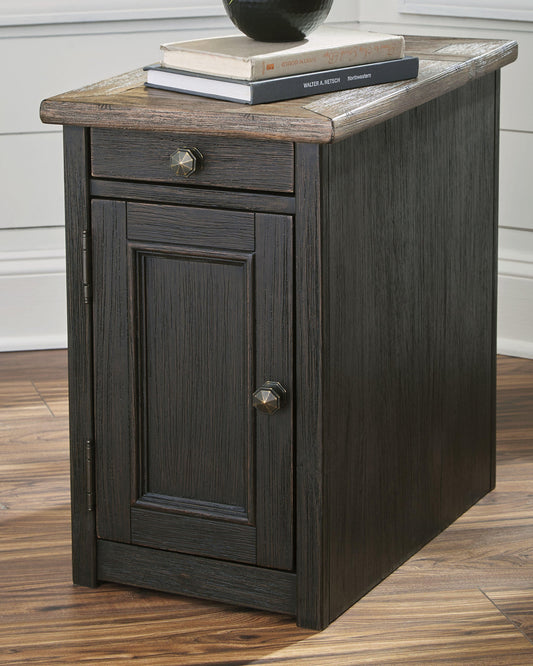 The Tyler Creek Chair Side End Table, finished in weathered gray-brown with a cabinet door and drawer, features a discreet charging station—perfect for keeping your devices powered while books rest on top.
