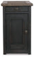 The Tyler Creek Chair Side End Table features a weathered gray-brown rustic finish, dark wood, round metal knobs, a top drawer, lower door, and a built-in charging station for added convenience.