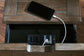 A smartphone charges via a USB cable connected to a power outlet inside the open drawer of the Tyler Creek Chair Side End Table, providing a convenient charging station.