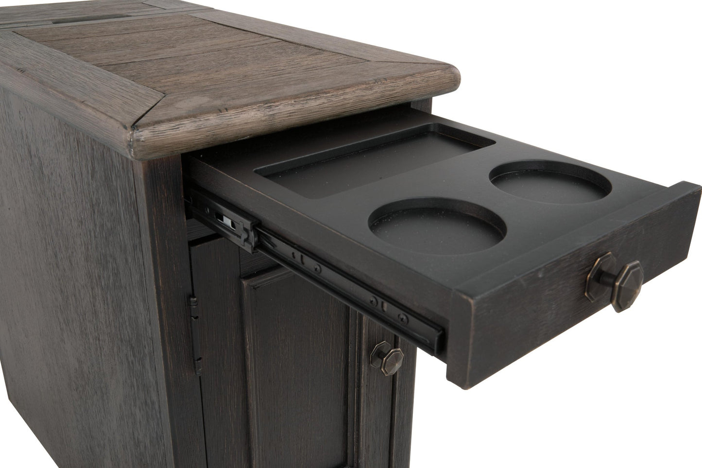 The Tyler Creek Chair Side End Table is a weathered gray-brown cabinet with a slide-out tray holding two cup holders, a rectangular slot, and a built-in charging station for added convenience.