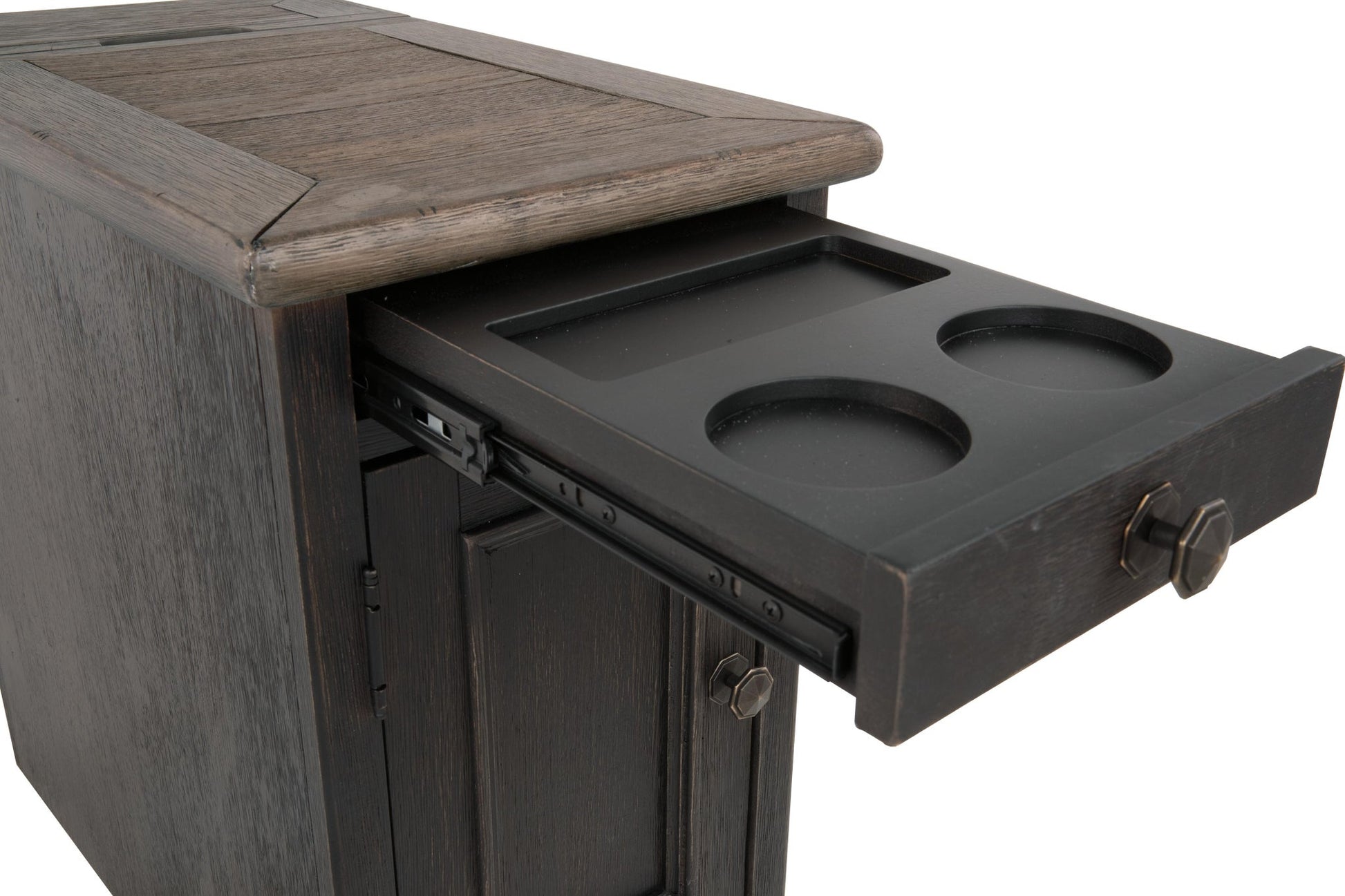 The Tyler Creek Chair Side End Table is a weathered gray-brown cabinet with a slide-out tray holding two cup holders, a rectangular slot, and a built-in charging station for added convenience.