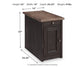 The Tyler Creek Chair Side End Table features a weathered gray-brown finish, one drawer, cabinet, and built-in charging station. Dimensions: 23"H x 14"W x 24.25"D; weight: 41 lbs. Measurements are shown with arrows.