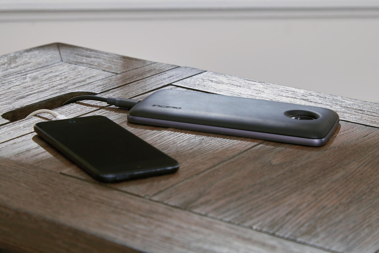 A black smartphone connected to a slim portable power bank via a charging cable rests on the Tyler Creek Chair Side End Table.