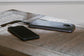A black smartphone connected to a slim portable power bank via a charging cable rests on the Tyler Creek Chair Side End Table.