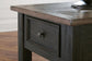 Close-up of the Tyler Creek Rectangular End Table, displaying a weathered gray-brown top and single drawer with a black knob, set on a hardwood floor.