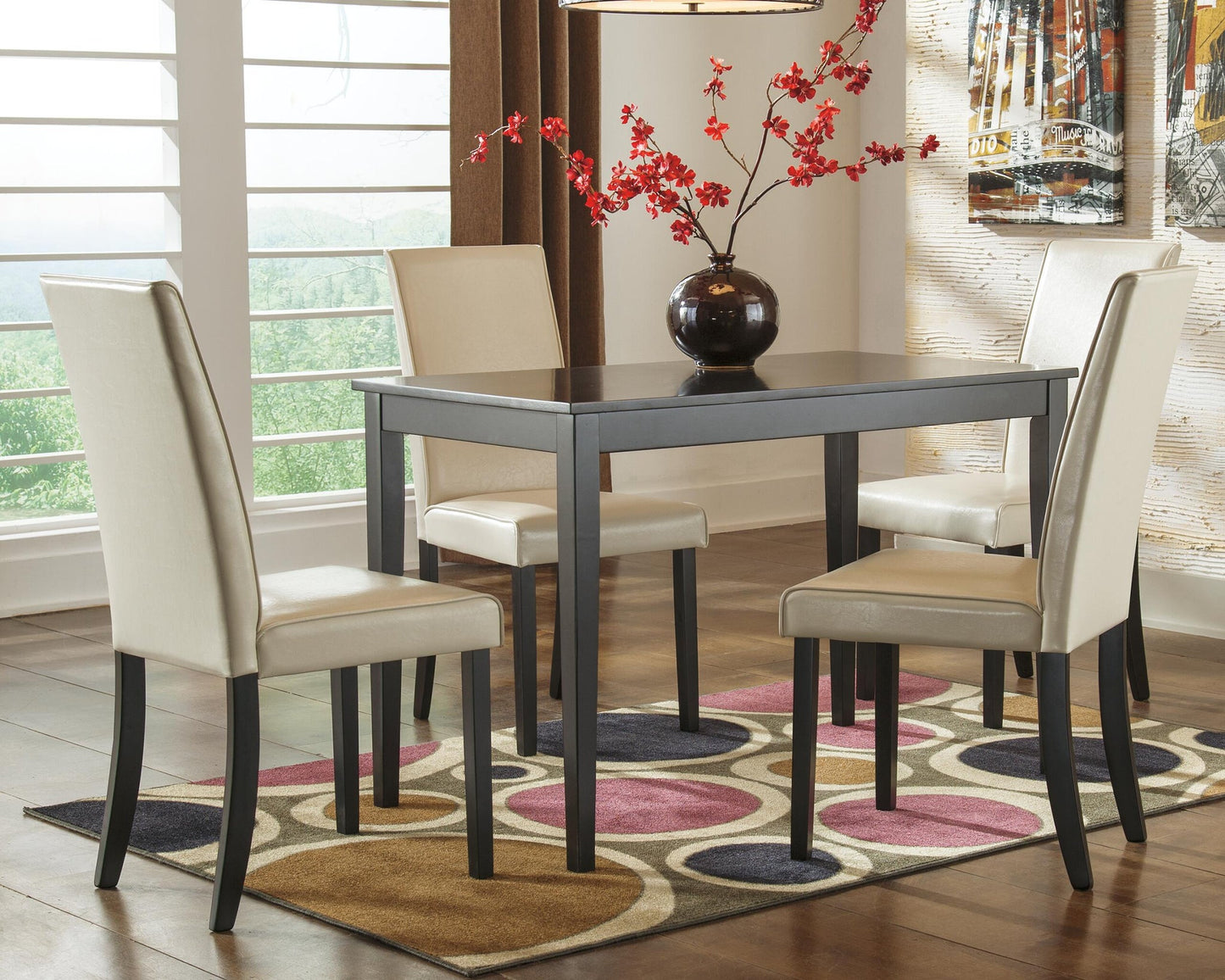 The Kimonte Rectangular Dining Room Table, paired with four beige chairs, a vase of red flowers, and a patterned rug, adds a stylish contemporary touch to this modern dining room.
