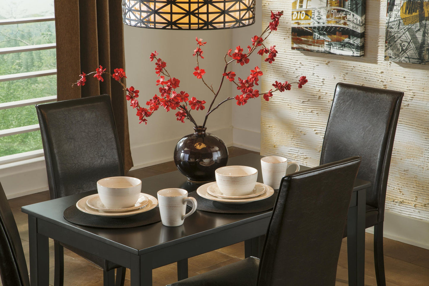 The Kimonte Rectangular Dining Room Table, paired with four black chairs, is set with plates, bowls, mugs, and features a dark vase with red flowers as a centerpiece under a geometric pendant light.