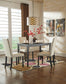 A modern dining room featuring the Kimonte Rectangular Dining Room Table set for four, cream chairs, a geometric pendant light, wall art, and a vase with red branches on a patterned rug.