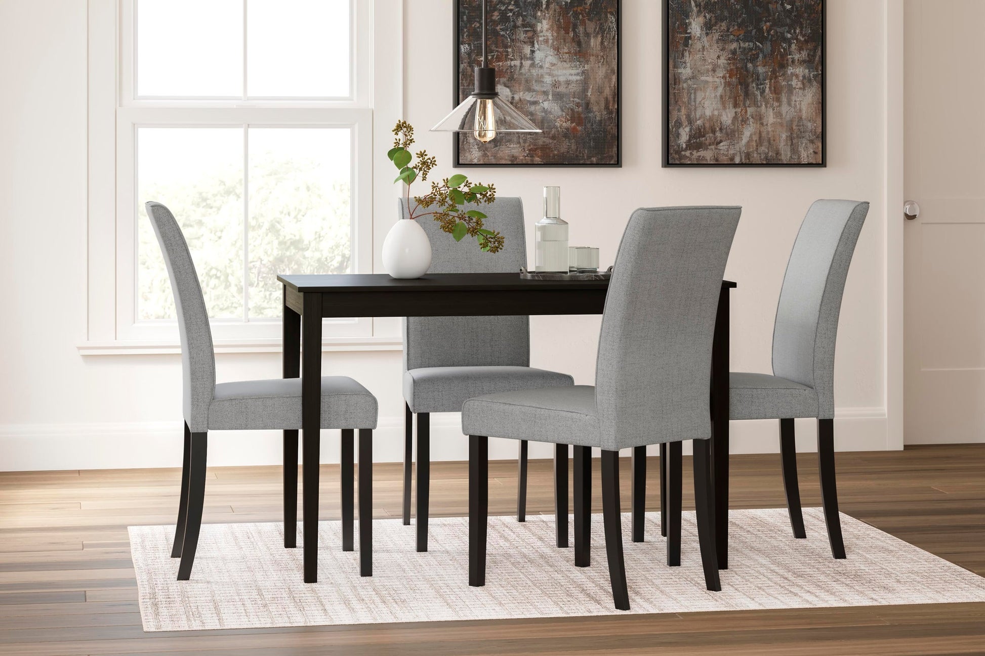 A modern dining room featuring the Kimonte Rectangular Dining Room Table in dark brown, four light gray upholstered chairs, a white vase with greenery, glassware, and two abstract wall paintings.